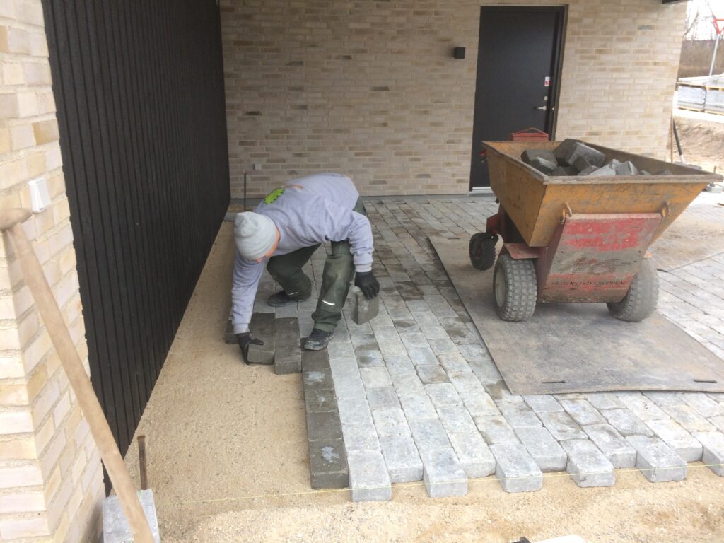 Anlægsgartner i gang med at lægge fliser i et område af en indkørsel.