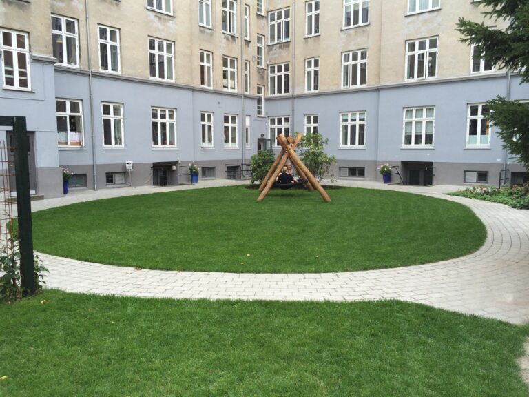 Grøn baggård i boligforening Lys og åben baggård i boligområde. Græsplæne omgivet af en cirkelformet stenbelagt sti